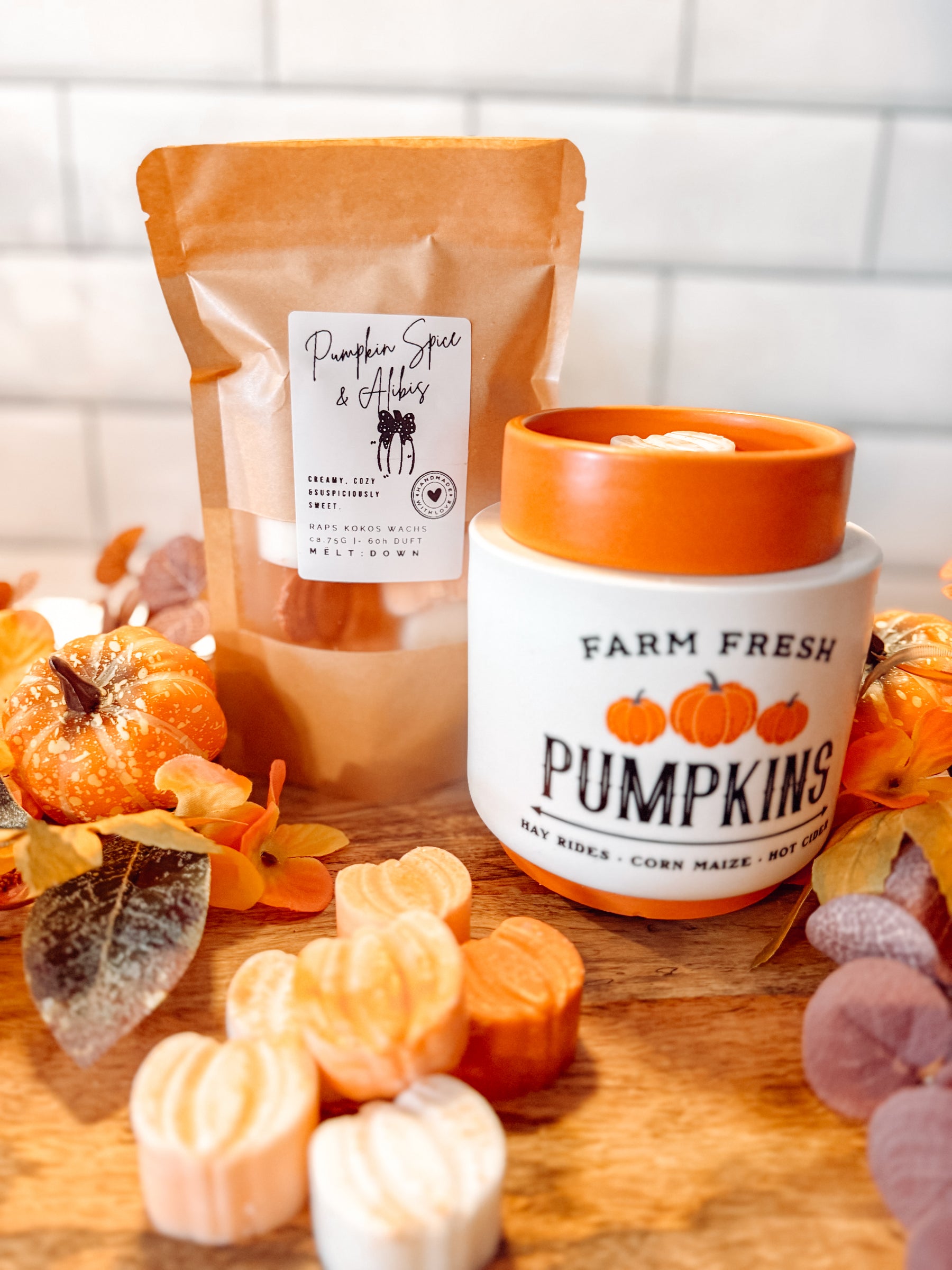 Pumpkin Spice & Alibis Duftwachs mit Kürbis-Icons neben einer orangefarbenen Duftlampe und Herbstdekoration