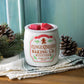 Gingerbread-Cookie-Duftlampe mit roten Wachswürfeln vor türkisfarbenem Hintergrund, daneben Tannenzweige und Zapfen.