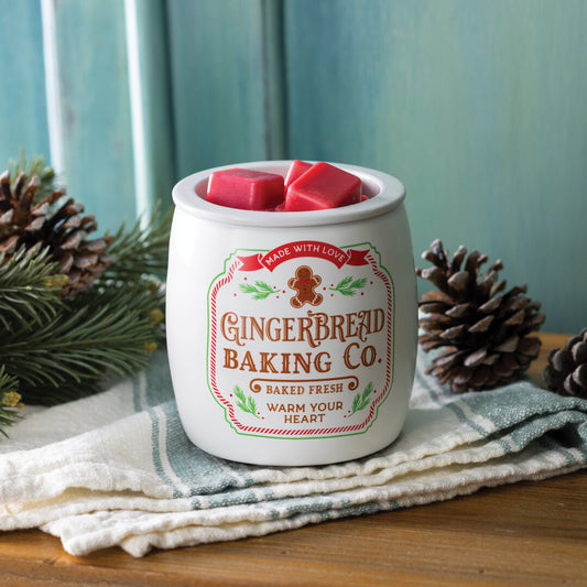 Gingerbread-Cookie-Duftlampe mit roten Wachswürfeln vor türkisfarbenem Hintergrund, daneben Tannenzweige und Zapfen.